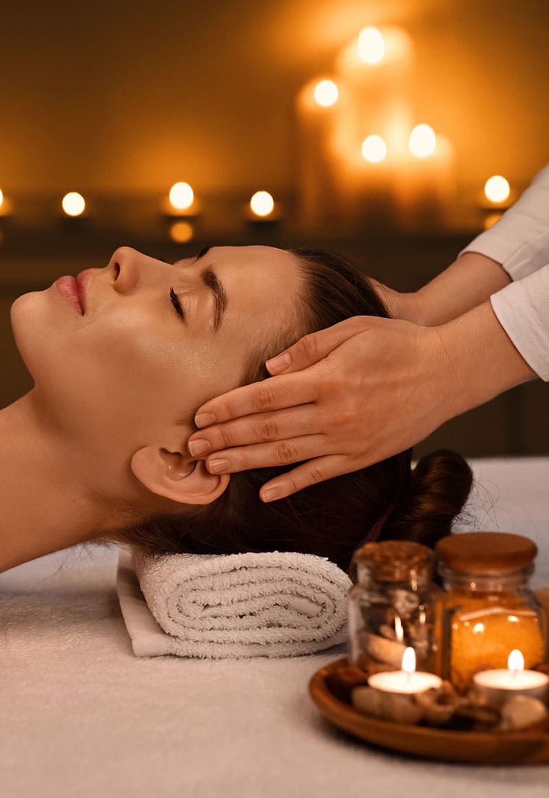 Relaxed young woman getting head massage at romantic spa atmosphere